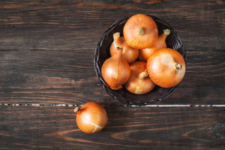 Raw golden onions in a basket on the wood tableの写真素材