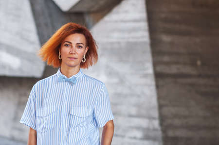 beautiful redhead girl wearing in a striped shirt posing against background of concrete wall
