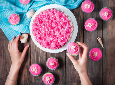 Woman's hands. Cake and cupcakes with pink cream on blue wood background. Top viewの写真素材