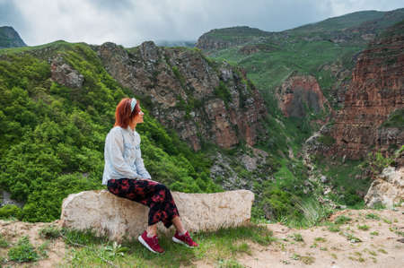 Female with red hairs enjoing stunning landscape of mountains. Dark clouds on the sky.の写真素材