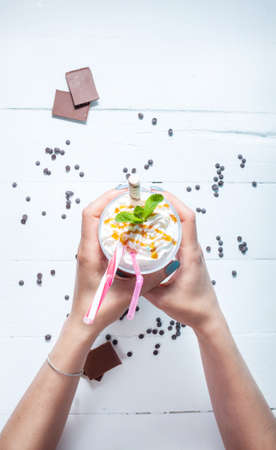 Woman hands and Homemade milkshake with caramel on white wooden table. Top viewの写真素材