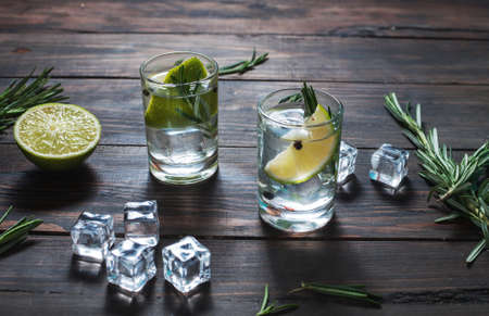 Alcoholic drink - gin tonic cocktail - with lime, rosemary and ice on rustic wooden table