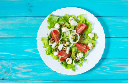 Caprese salad. Cherry-tomatoes, baby spinach and mozzarella in metal bowl with pesto dressing on rustic wooden backdrop, top viewの写真素材