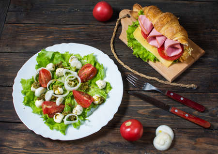 Light and hearty spring breakfast. Croissant with ham, cheese, fresh tomatoes and salad with Mozzarella on a wood tableの写真素材