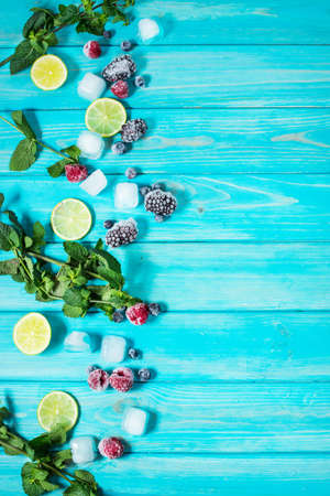 fresh berries, lime, mint and ice cubes on blue wood background top view. Copyspaceの写真素材