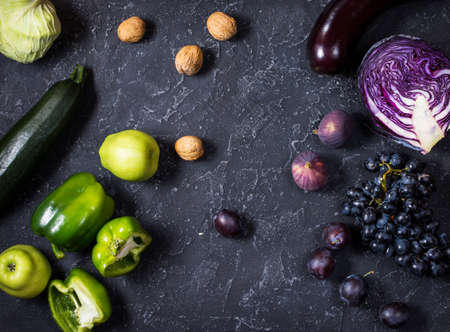 Fresh organic raw green and purple colored vegetables and fruits on dark stone background.の写真素材