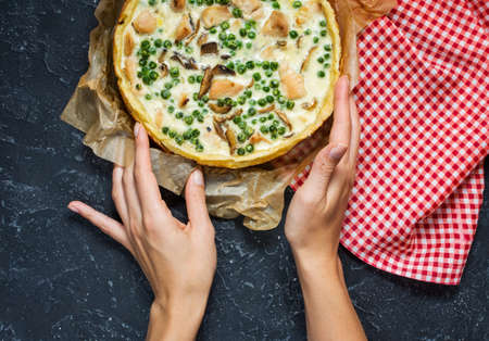 Fresh chicken pie with cheese on dark stone background. French quiche. Homemade tart. Female hands. Top viewの写真素材