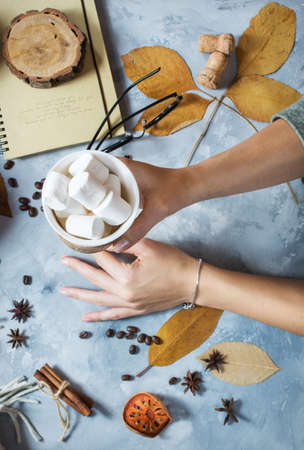 Autumn background with cup of marshmallow, yellow maple leaves and pumpkins. women's hands hold a cup. Top viewの写真素材