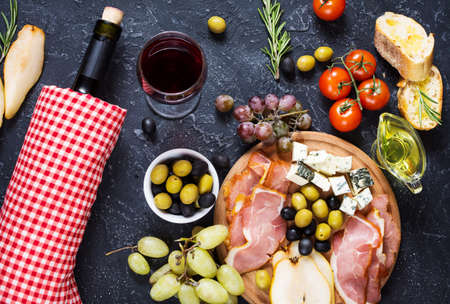Appetizer, italian antipasto, ham, olives, cheese, bread, grapes, pear and wine on dark stone background Top viewの写真素材