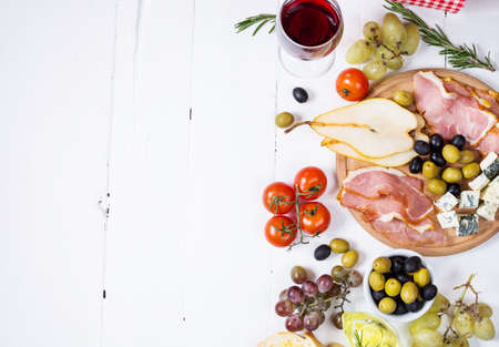 Appetizer, italian antipasto, ham, olives, cheese, bread, grapes, pear and wine on white wood background. Top view copy spaceの写真素材