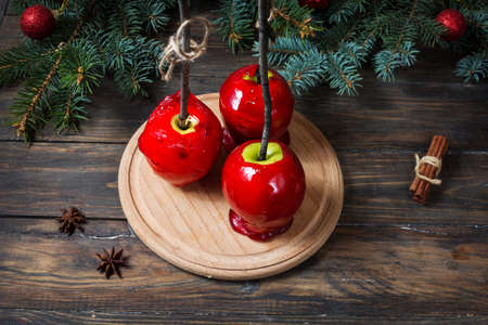 Red caramel apples on sticks on Dark wood background, with Christmas tree branches.の写真素材