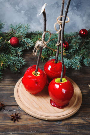 Red caramel apples on sticks on Dark wood background, with Christmas tree branchesの写真素材