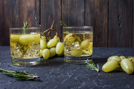 Two glasses of green grape juice with fresh fruits and rosemary on dark stone background.の写真素材