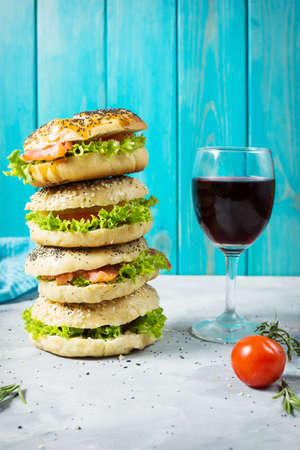 Heap of Bagels with salmon, vegetables, cream-cheese and glass of red wine on grey concrete...