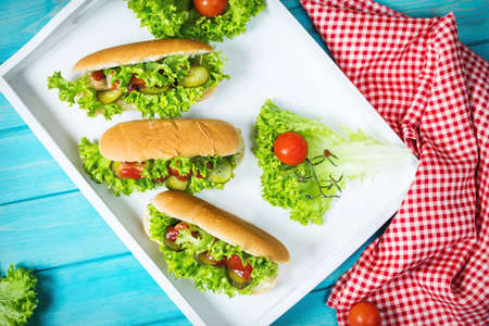 Hot dog with pickles, tomato and lettuce on blue wooden background. Top view.