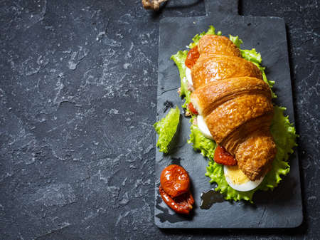 Croissant sandwich with tuna, hard boiled egg, salad and sun-dried tomatoes on stone table. Copy spaceの写真素材