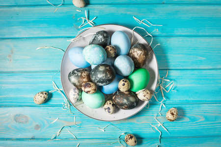 painted eggs on plate, quail and chicken eggs, paint and brush on blue wood background, Easter decorations.の写真素材