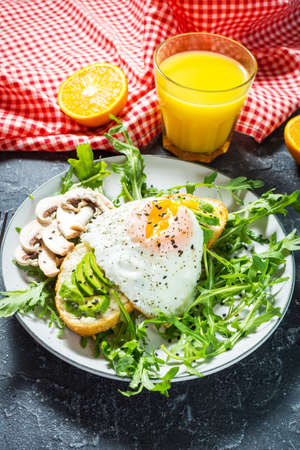 Tasty sandwiches with avocado and egg, arugula on a dark plate on white wooden background. Delicious...