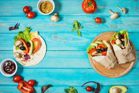 Healthy vegan lunch snack. Tortilla wraps with mushrooms, fresh vegetables and Ingredients on blue wooden background. Top viewの写真素材