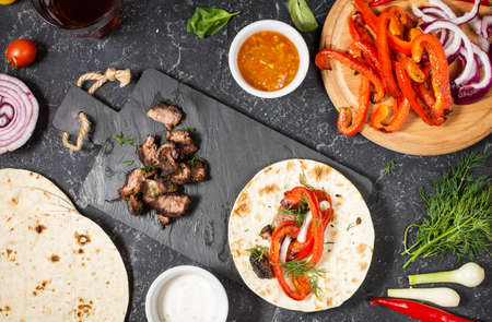Fresh delicious mexican tacos and food ingredients on black stone background. Cooking. Top viewの写真素材