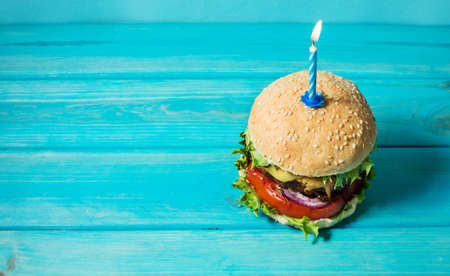 Homemade burger barbeque sandwich with beef and lit candle for birthday party on blue background....