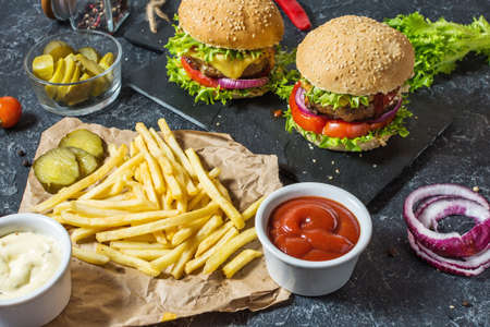 Two beef burgers, fries potatoes and cucumber on dark stone table.の写真素材