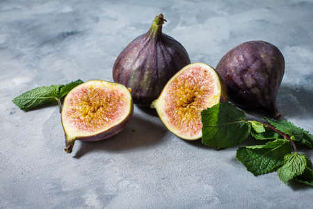 Ripe sweet figs with green leaves on concrete background.