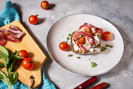 Sandwich with cherry tomatoes and prosciutto on plate over concrete backgroundの写真素材