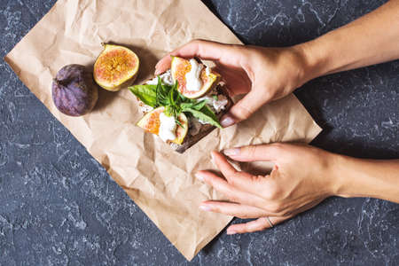 Female hands hold figs fruit sandwich on a black stone backgroundの写真素材