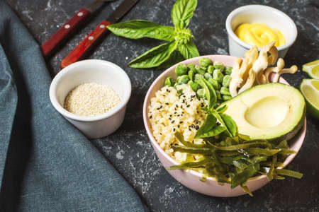 Buddha bowl recipe with quinoa, avocado, lentils, mushrooms, sea kale on black stone background.