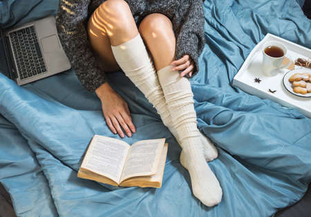 Beautiful Legs close-up in bed, girl with a cup of tea and reading a bookの写真素材