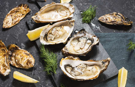 Opened Oysters with lemon on dark stone texture backgroundの写真素材