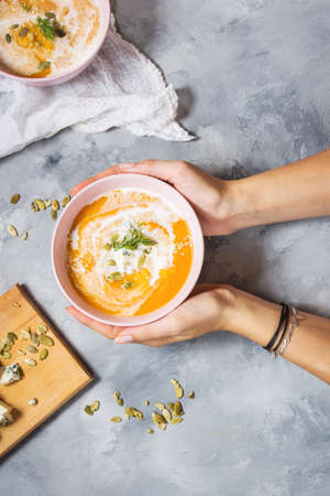 Female hands holding a bowl of pumpkin soup on concrete background. Top viewの写真素材