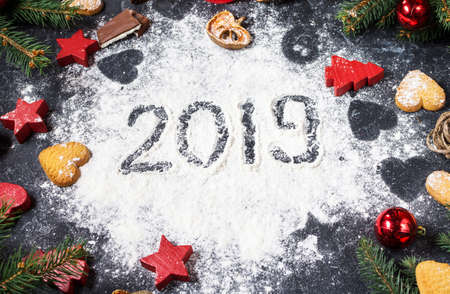 Happy New Year 2019 written on flour and Christmas Decorations Gingerbread cookies on dark stone background. New Year greeting cardの写真素材
