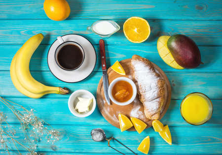 Breakfast served with coffee, orange juice, croissants and fruits on blue wood backgroundの写真素材