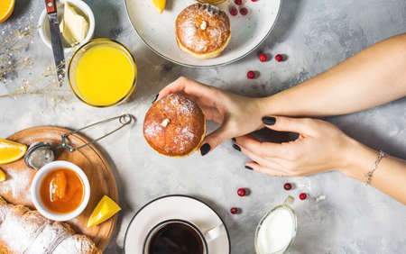 Female hands hold donut. Breakfast served with coffee, orange juice, croissants and fruits on concrete background. Top viewの写真素材