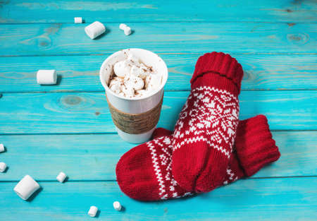 hot chocolate with marshmallow and red mittens on blue wooden table.