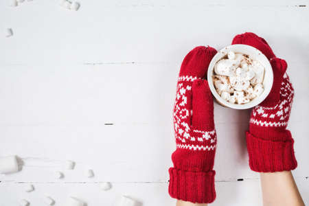 Female hands holding hot chocolate with marshmallow above white wooden table. Top view and copy spaceの写真素材