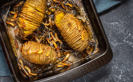 Roasted hasselback potato on cast iron pan. Dark background
