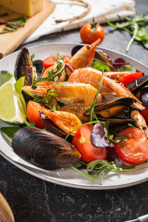 Fresh seafood salad, mussels, shrimp, fresh vegetables and herbs on black stone backgroundの写真素材