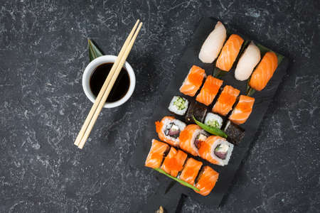 Various kinds of sushi rolls served on black stone background. Top view
