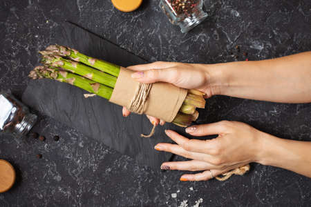 Female hands hold banches of fresh green asparagus on stone backgroundの写真素材