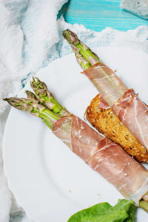 Fresh Young Asparagus Wrapped in Prosciutto Meat on a blue wood table.の写真素材