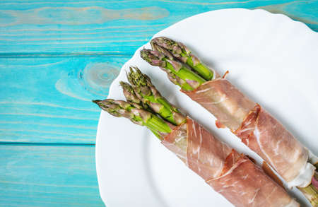 Fresh Young Asparagus Wrapped in Prosciutto Meat on a blue wood table. Top viewの写真素材