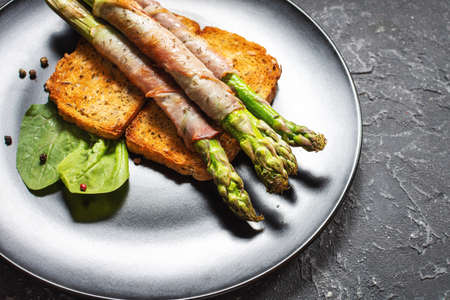 Grilled green asparagus wrapped with bacon on toastsの写真素材