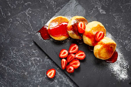 Russian syrniki or cottage cheese fritters or pancakes served with strawberry on black stone background. Top viewの写真素材