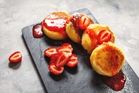 Russian syrniki or cottage cheese fritters or pancakes served with strawberry on concrete background. Breakfastの写真素材