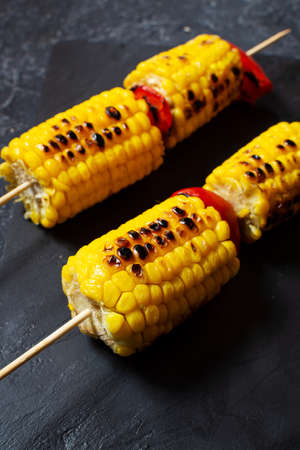 Grilled sweet corn on the sticks, black stone textured table