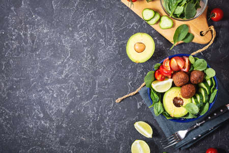 Salad with avocado, falafel, cucumber, cherry tomato and spinach on black stone background. Healthy vegan lunch bowl. Top view and copy spaceの写真素材