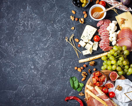 Italian antipasto with prosciutto, ham, cheese, olives and grissini breadsticks on black stone background. Top view and copy spaceの写真素材